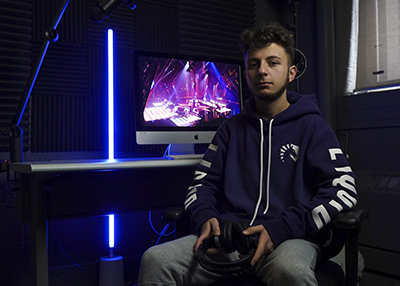 Hisham Almadani holds a gaming controller while sitting in a dark room, with the only light coming from a computer.