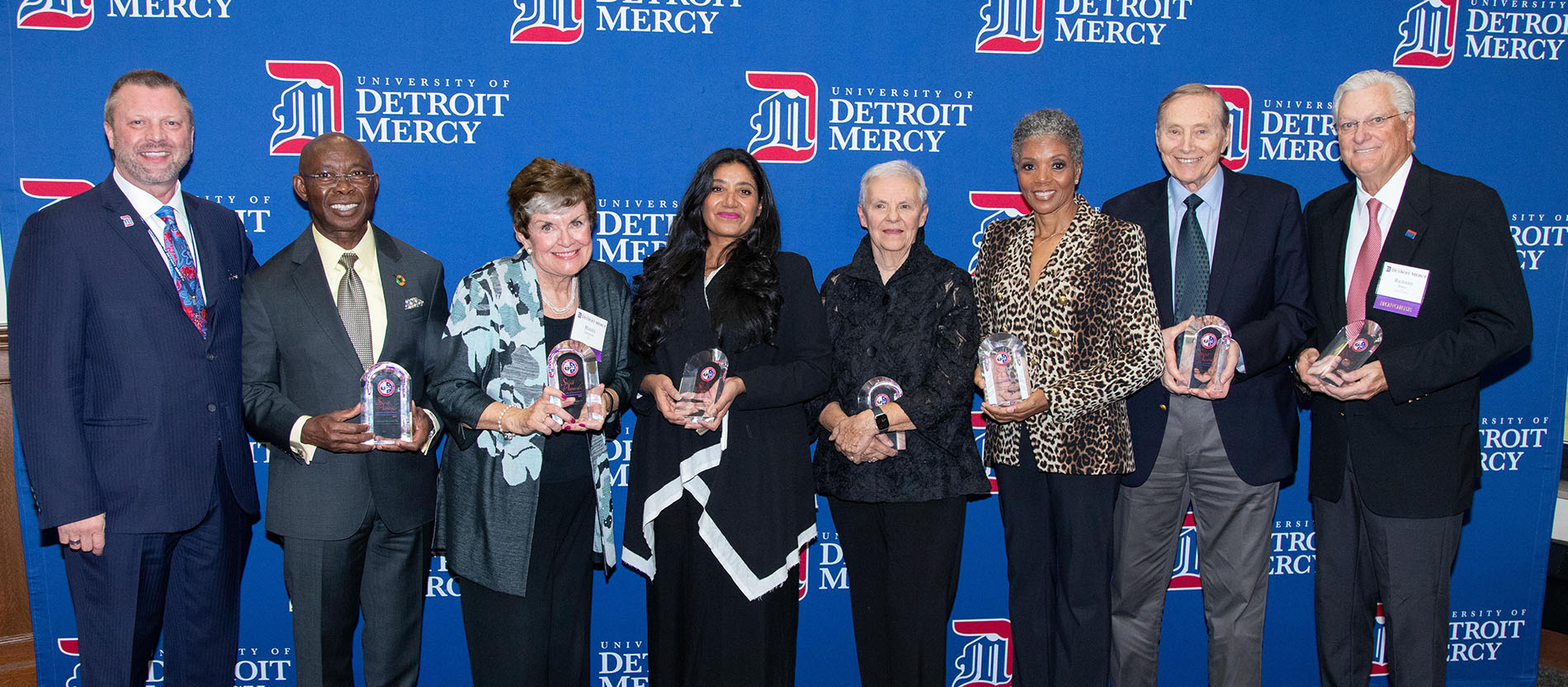 President Taylor poses with the seven Spirit Award winners in front of a blue University of Detroit Mercy banner.