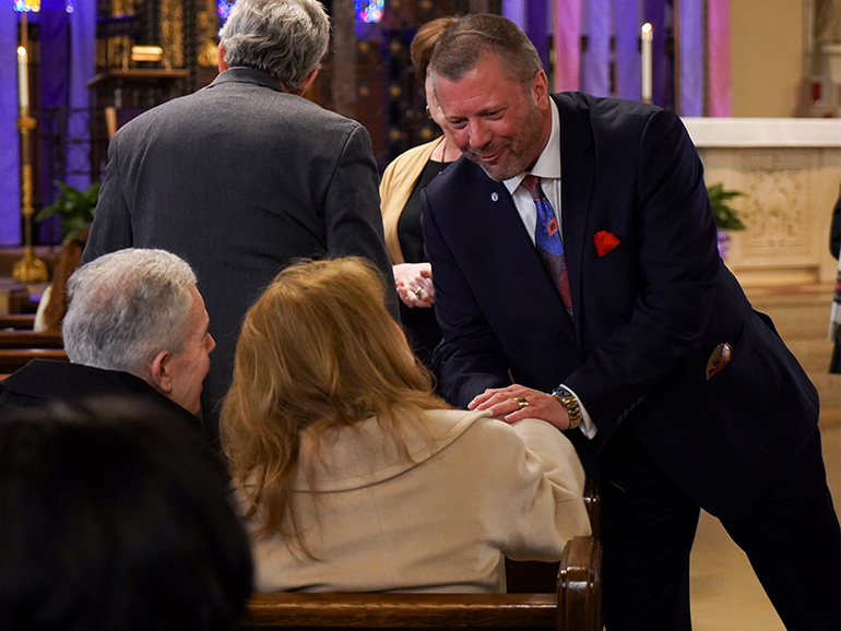 A man shakes hands with two people sitting in a pew of a church.