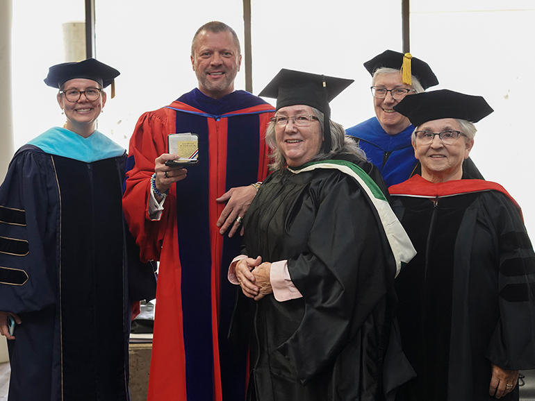 Five people wearing robes stand and smile for a photo, with one person holding a medallion.