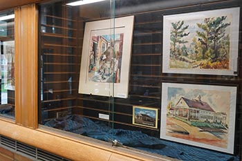 Several of Pauline Locher's paintings are on display at the McNichols Campus Library, including paintings of a forest area and a building. 