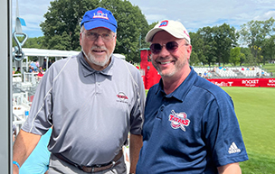 Two people stand outside in a suite at the Rocket Mortgage Classic golf tournament.