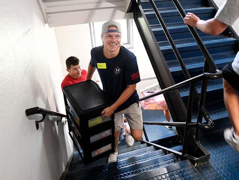 Two students smile as they bring belongings up a staircase of Shiple Hall.