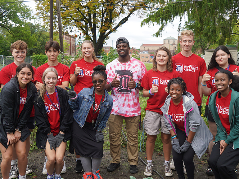 A dozen Detroit Mercy students wearing University of Detroit Mercy t-shirts pose for a photo while participating in community service.