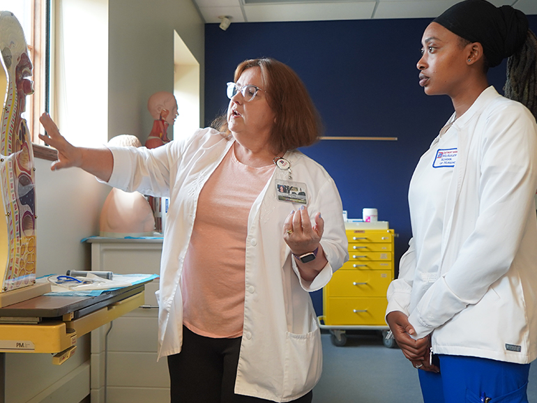 Two people stand inside of a classroom of the STAR Center and study an instructional tool of a human.