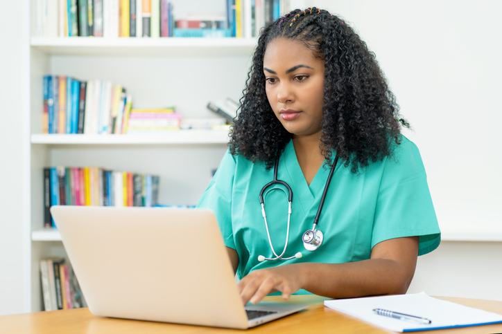 One person in nursing scrubs types on a laptop computer.