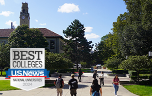 An outdoor photo of the McNichols Campus on a sunny day with students walking on campus amongst trees, buildings and a clock tower.