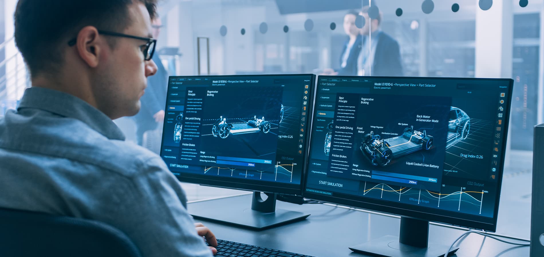 A stock photo of a man sitting at a desk with two computer monitors in front of him.