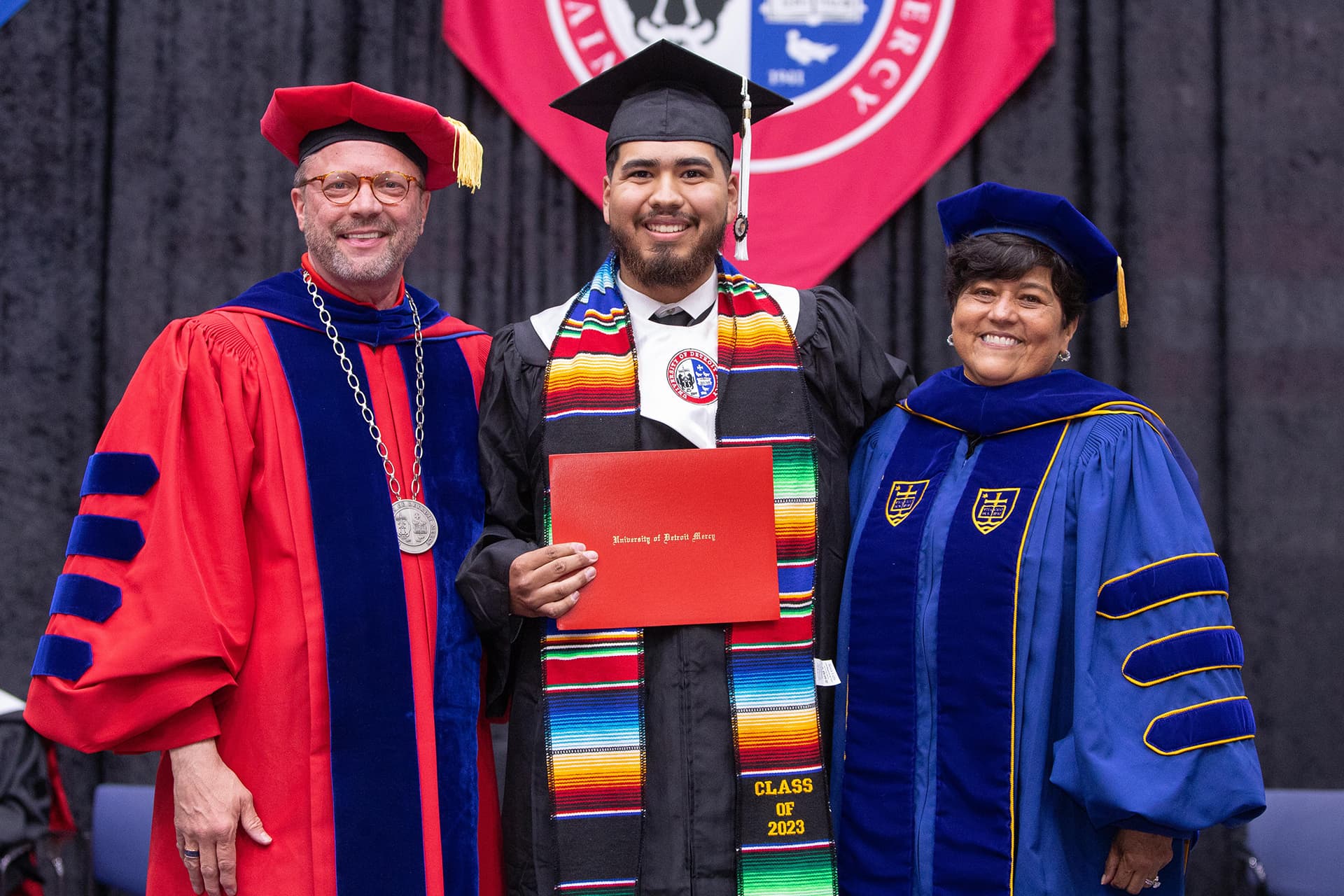 Three people pose for a photo during a commencement ceremony, wearing caps and gowns.