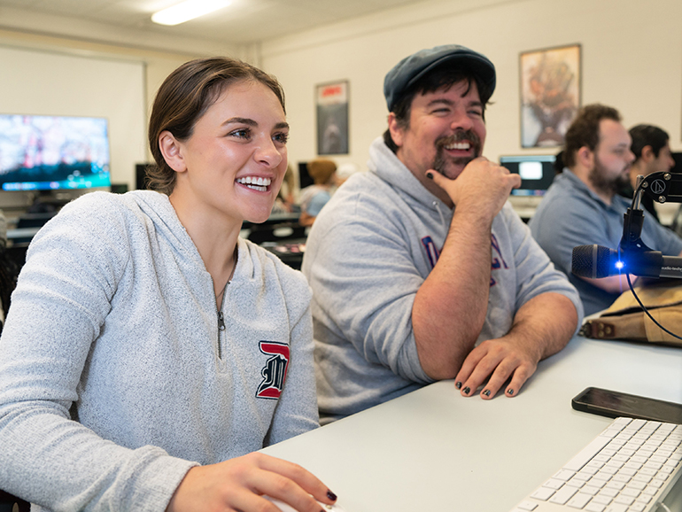 Kara Wolfbauer and a classmate share a laugh sitting inside of a classroom.