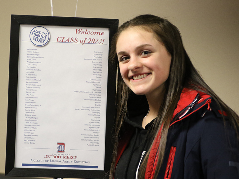 Kara Wolfbauer smiles next to a list of names on Accepted Students Day inside of a building.