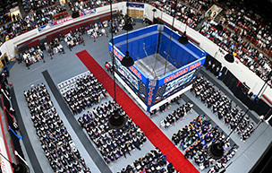 An aerial photo of hundreds of graduates and people sitting below inside underneath the Calihan Hall scoreboard.