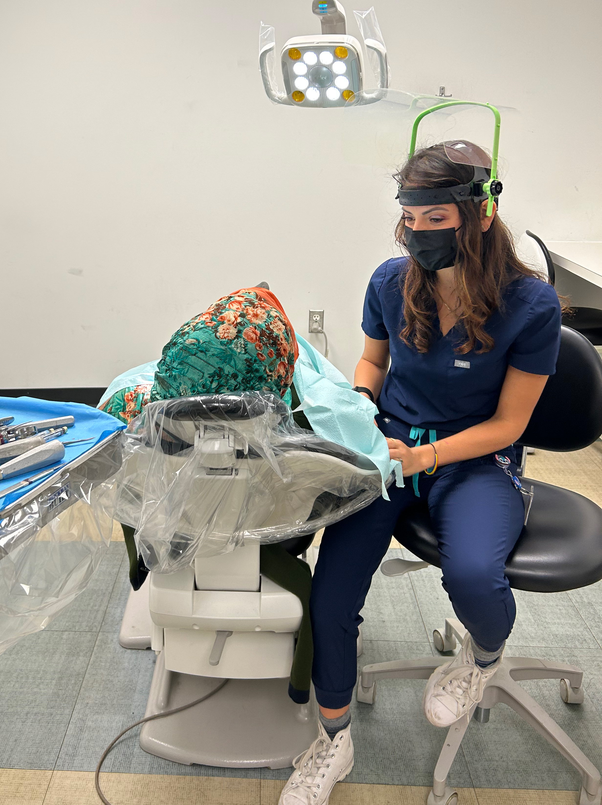 A dental student works on a patient that lies on a chair, inside of a medical room.