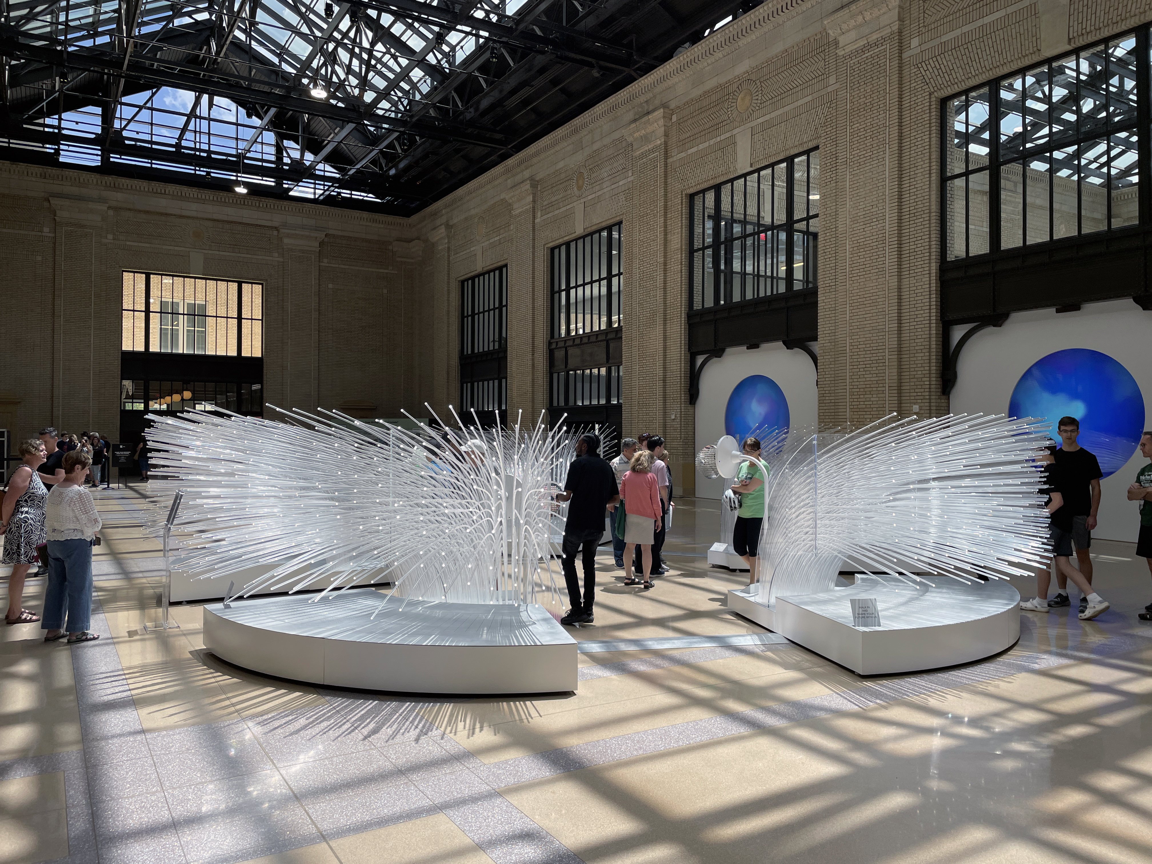 A photo of the me + you sculpture inside of Michigan Central Station, with people mingling about it.
