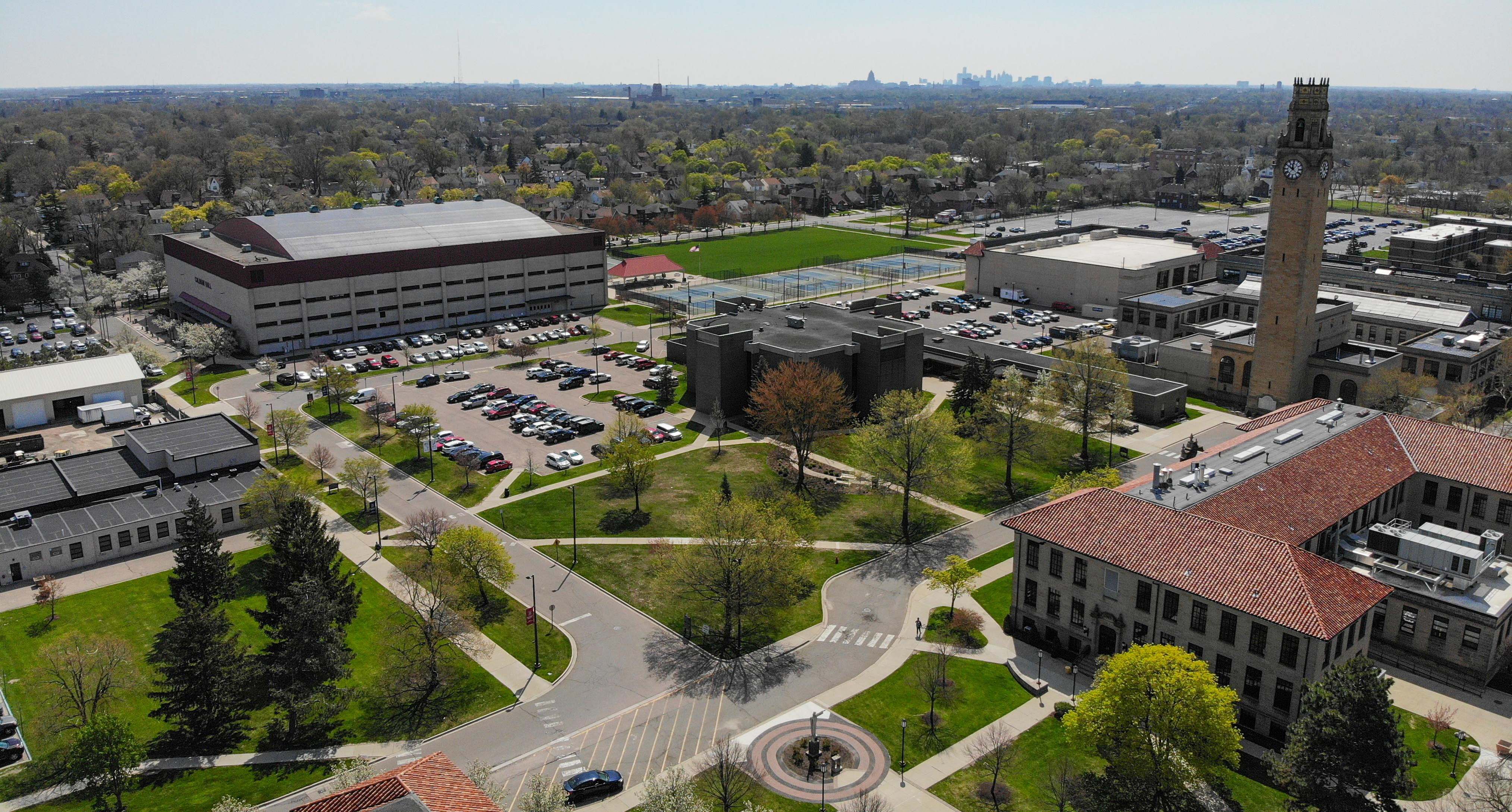 An aerial photo of Detroit Mercy's McNichols Campus on a sunny summer day, featuring buildings, trees, cars, houses and downtown Detroit in the background.