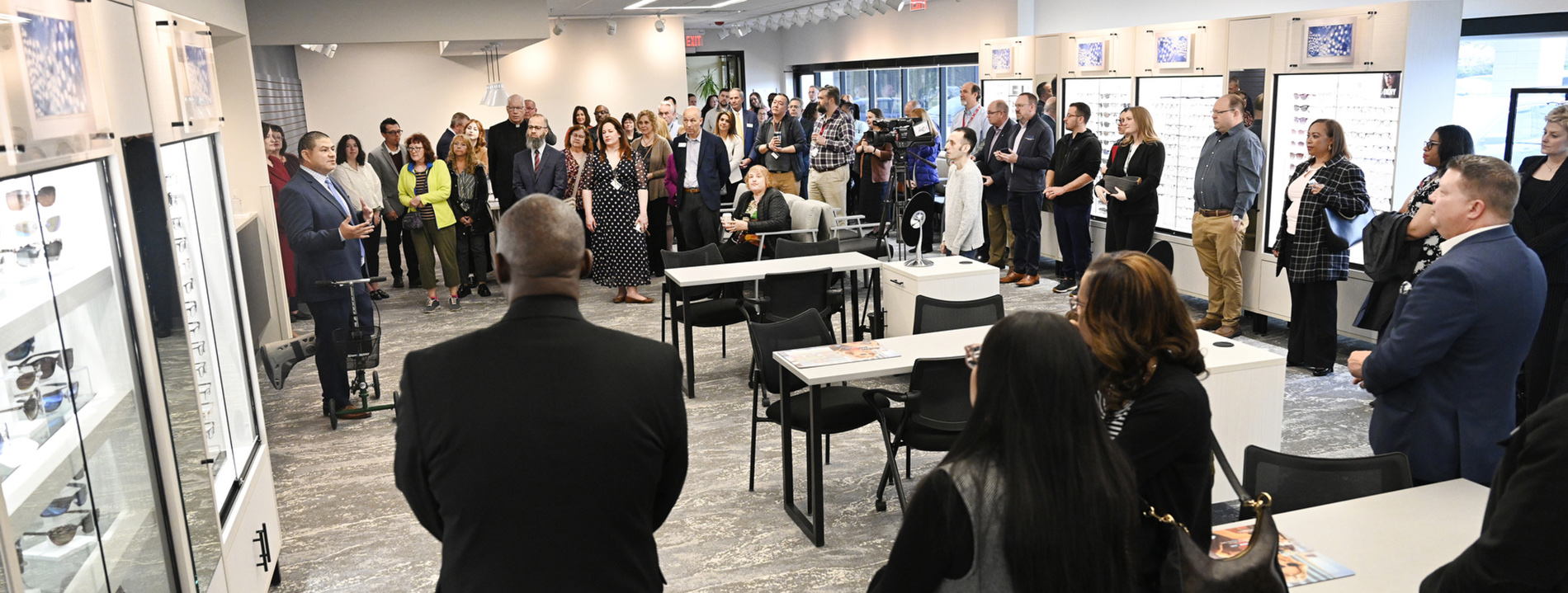 A person speaks at the Eye Institute opening while many people stand around the room listening.