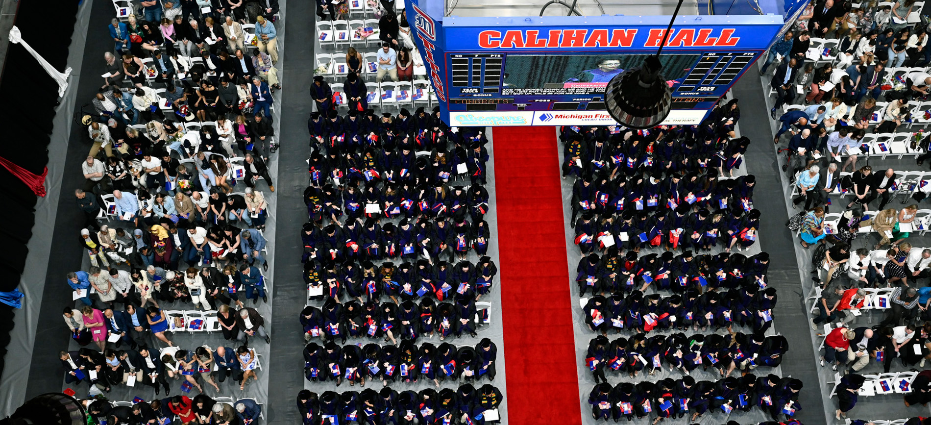 An overhead view of graduates and families seated in rows during commencement.
