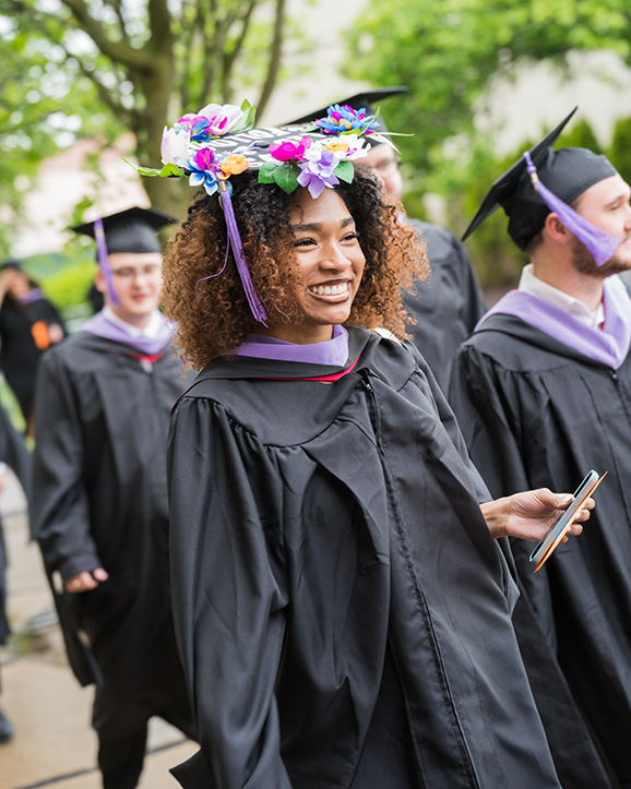 A graduate with a colorfully decorated grad cap processes into Calihan Hall during commencement..