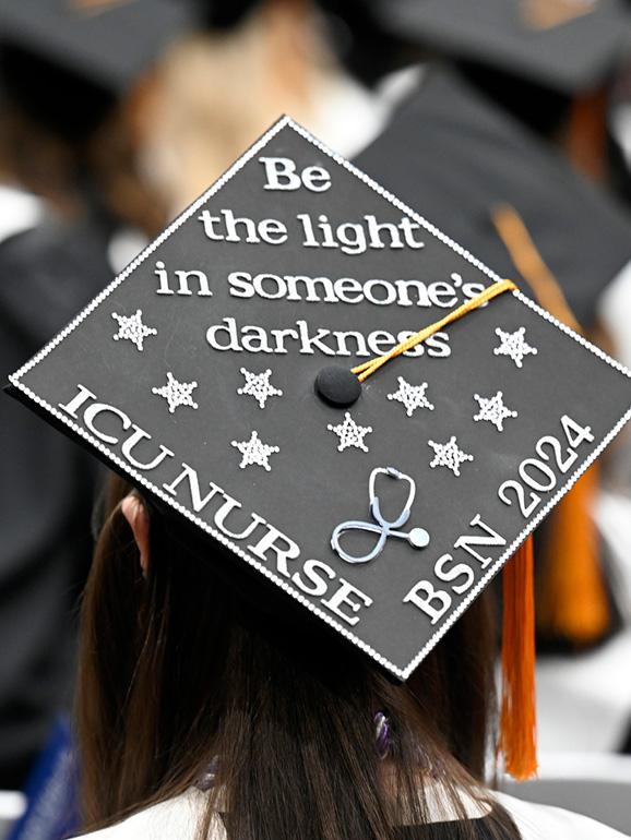 A decorated graduation cap with the text "Be the light in someone's darkness, ICU Nurse, BSN 2024" around silver stars.