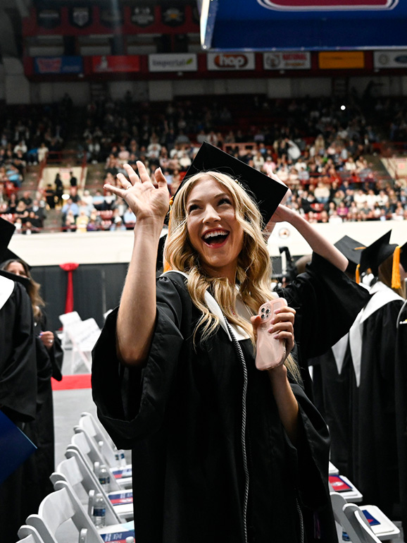 A graduate waves to people in the stands during commencement.