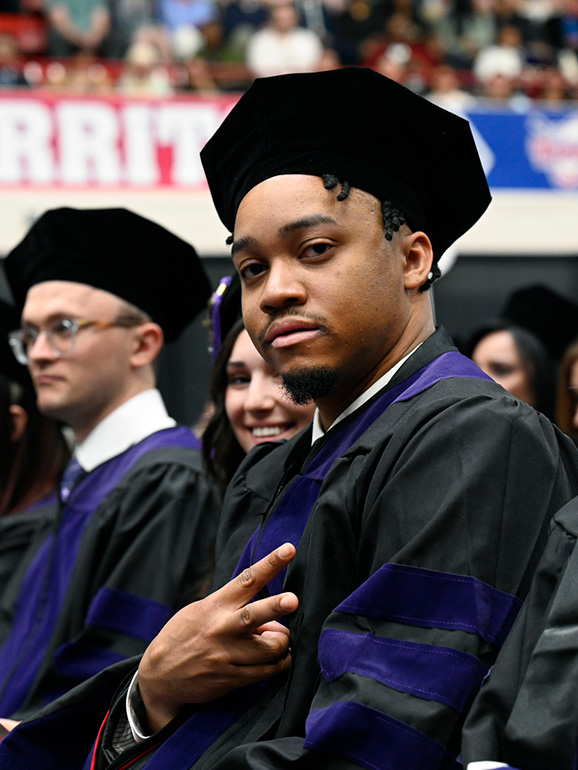 A graduate gives the peace sign while sitting during commencement.