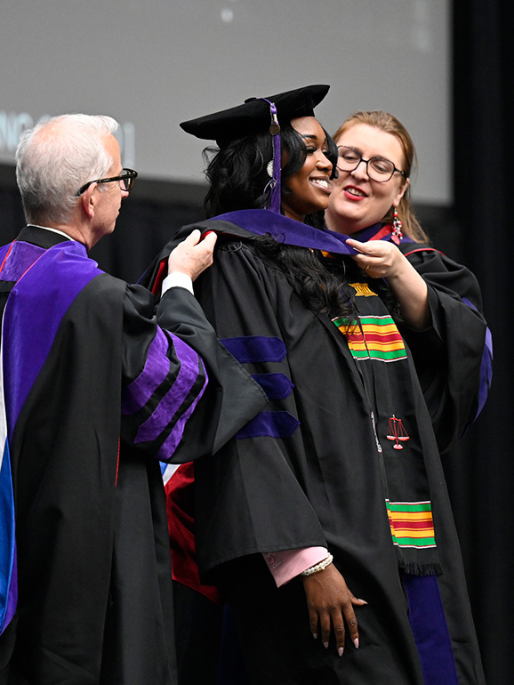 A graduate is hooded by two people during commencement.