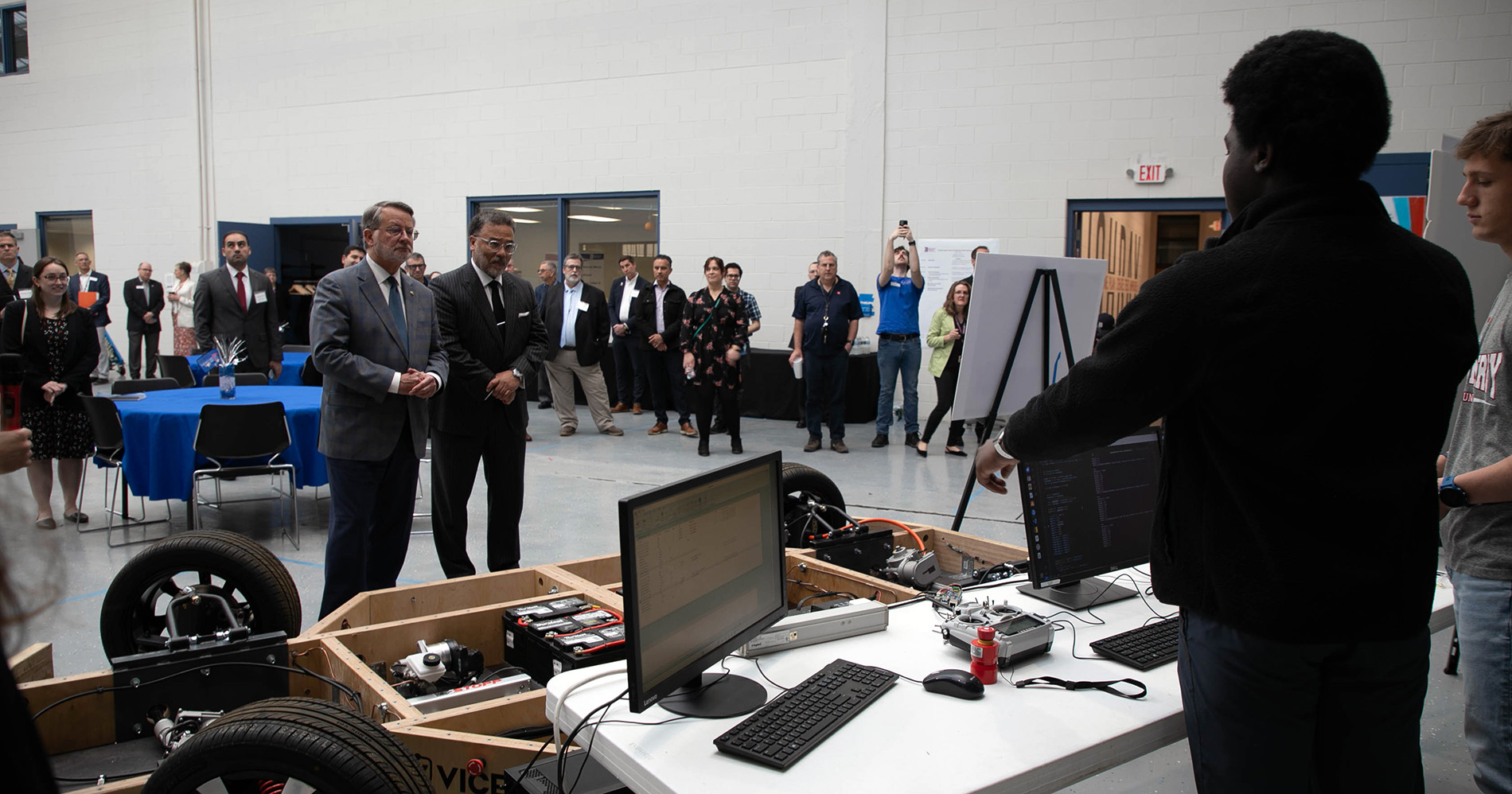 U.S. Sen. Peters and National Cyber Director Harry Coker Jr. watch students talk near a vehicle in the Engineering Building while others look on.