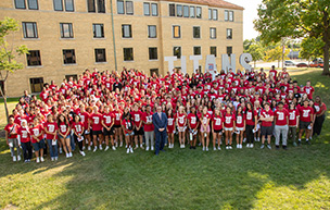 Dozens of new Titans in red shirts stand outdoors in front of the TITANS sign on the McNichols Campus.