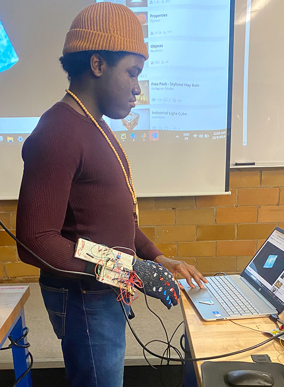 Agholor stands with a mechatronic hand next to a computer inside of a classroom.