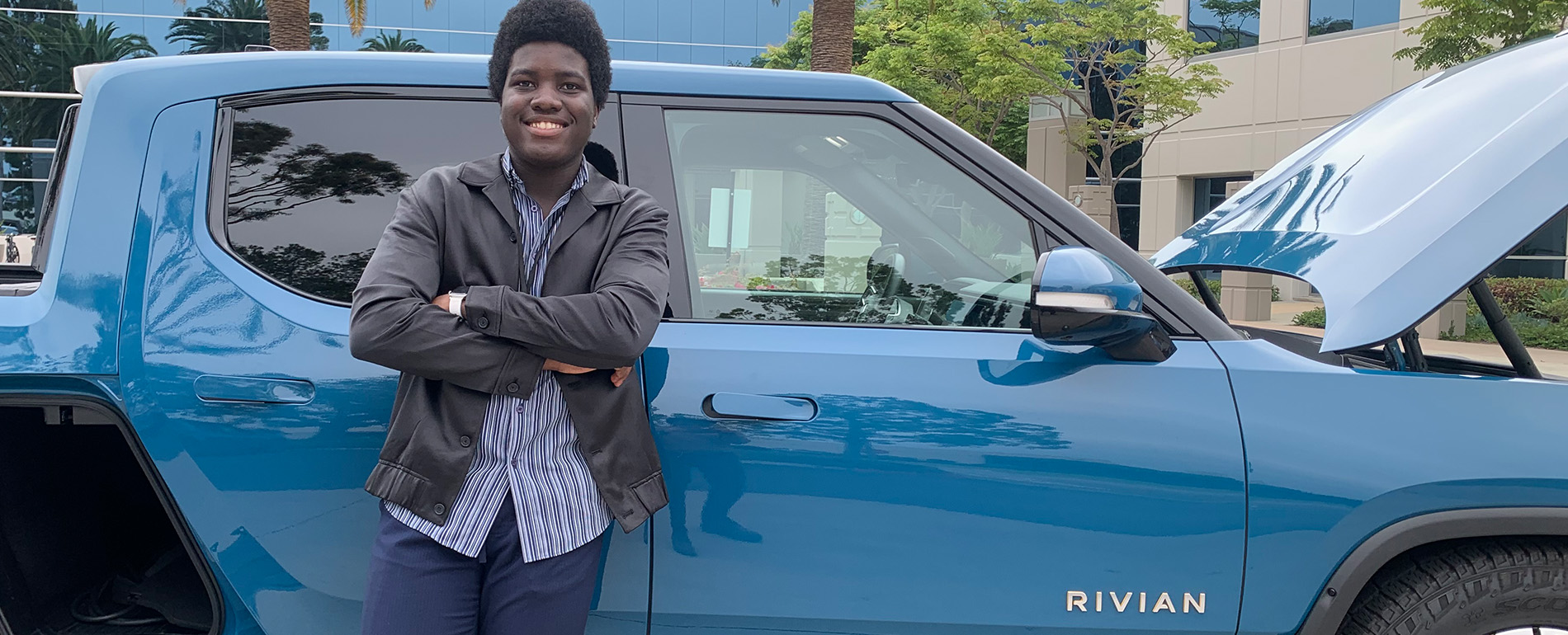 Oriekaose Agholor leans against a blue Rivian electric vehicle outdoors.