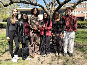 Zaynab Alhisnawi stands with her peers while holding an award.