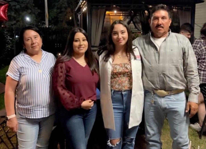 Four people stand and pose for a photo outdoors at night.