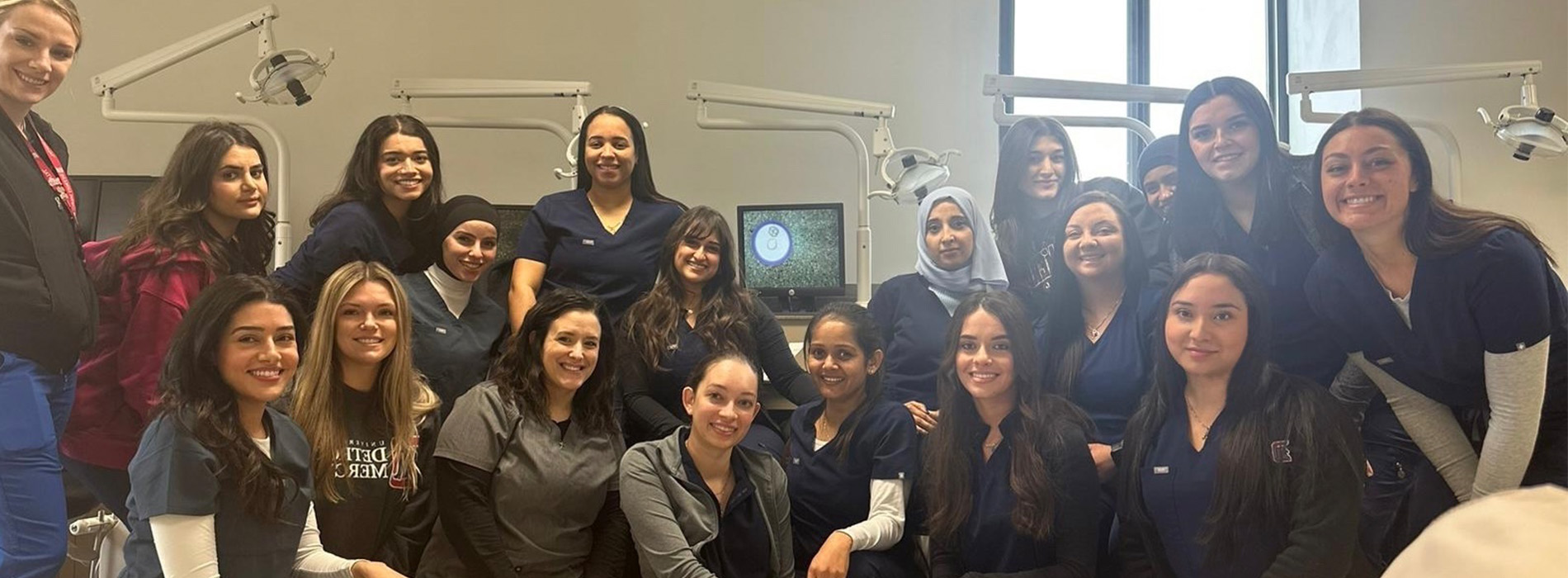 More than a dozen people in scrubs kneel and stand for a photo inside of a clinical setting at Detroit Mercy Dental.