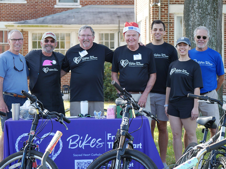 Seven people standing pose for a photo with a bicycle outdoors