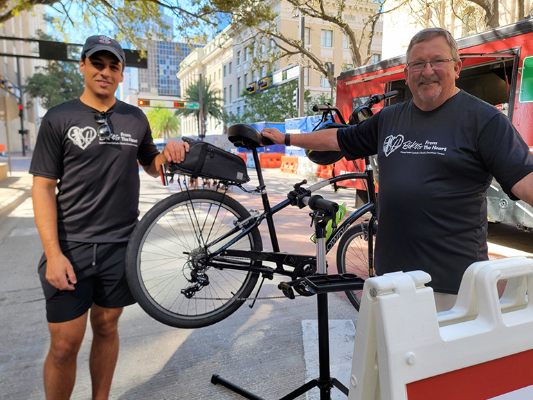 Two people pose outdoors with a bicycle in front of a van in downtown Tampa