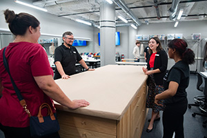 A faculty member stands next to a student who is operating a sewing machine during a Performing Arts class.