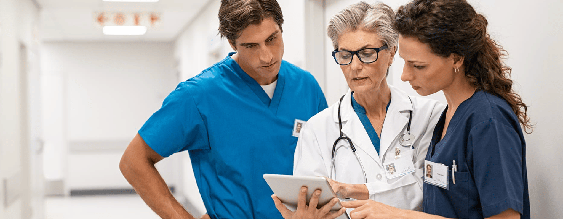 Three healthcare employees talk while looking at a tablet.