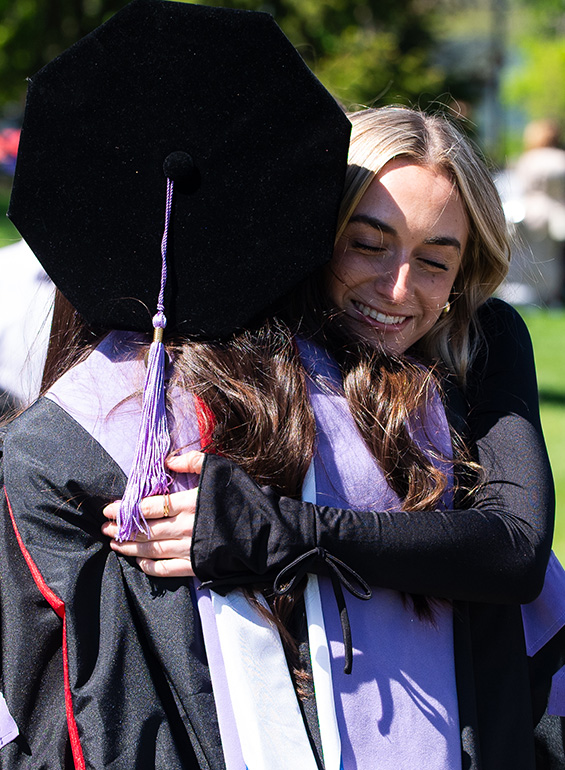 A graduate hugs someone outdoors following a ceremony.