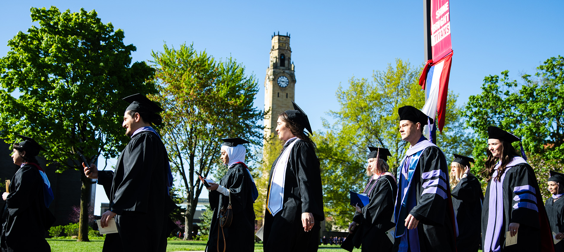 Students walk down the road in front of the clock tower outdoors.