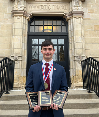 Mark Formosa holds a number of award plaques outside of the Commerce & Finance building.