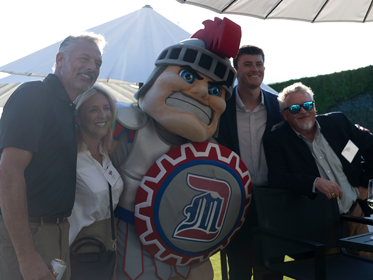 Four people pose for a photo with Tommy Titan, outdoors.