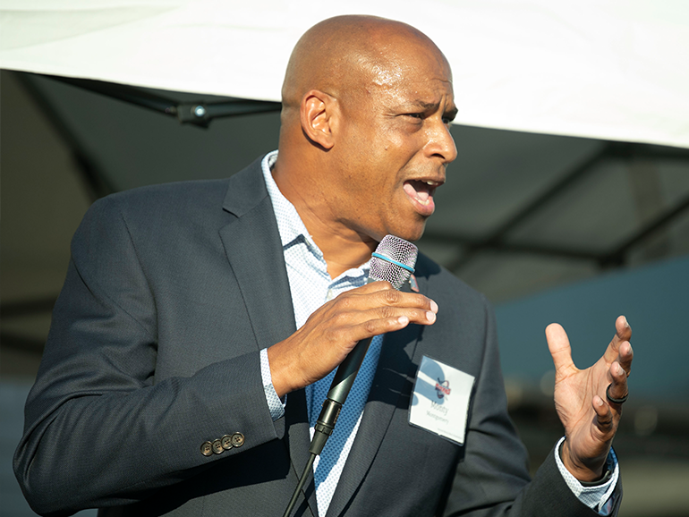 Mark Montgomery speaks outdoors with a microphone in his hand.