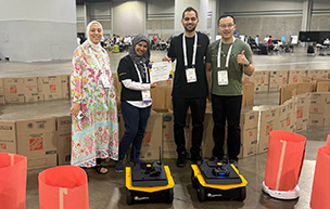 Four people stand behind a pair of robots.