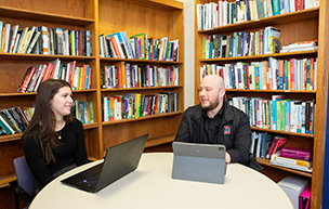 Two students sit at a table and talk.
