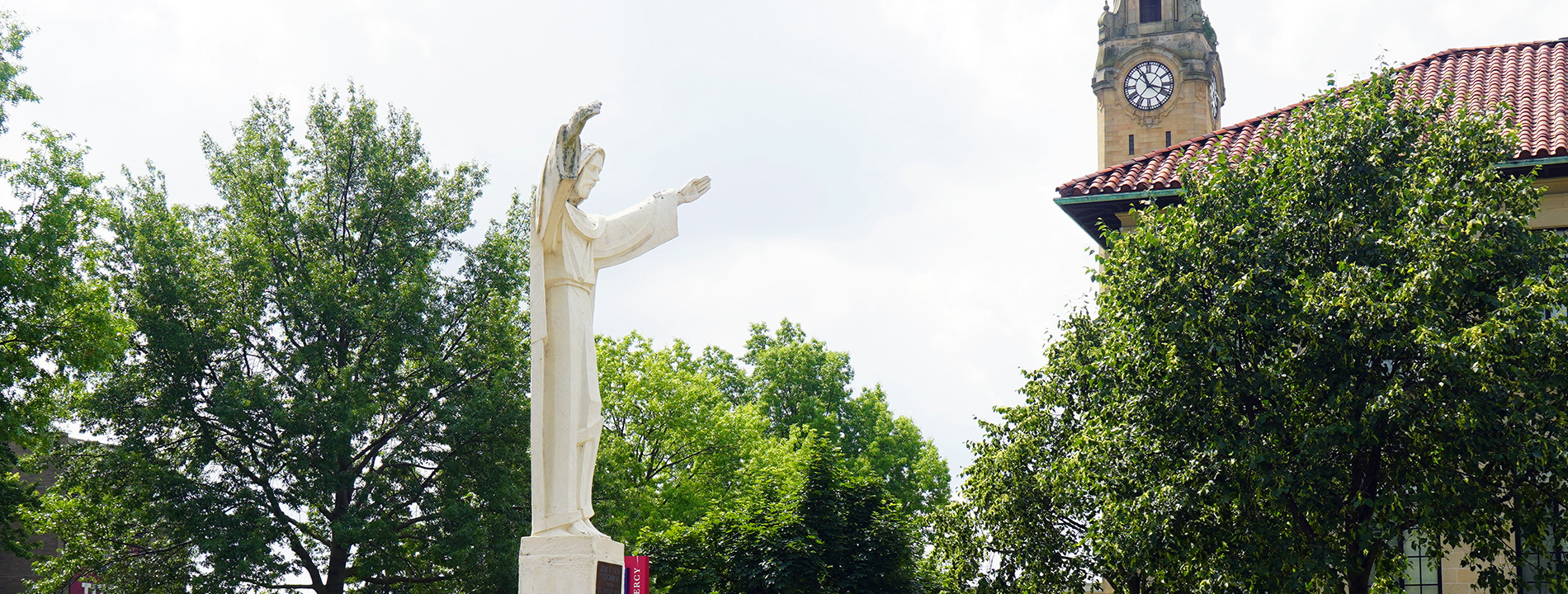 The Jesus statue, Chemistry building, trees and clock tower are visible during a summer day on the McNichols Campus.