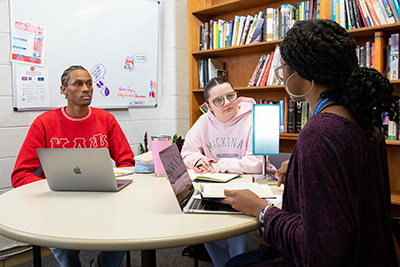 Students socialize at a table with their laptops.