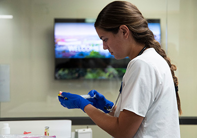 A student uses a needle to get medicine for a nursing sim.