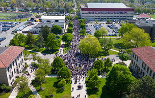 Hundreds of people fill the streets of the McNichols Campus amidst trees, cars and buildings.