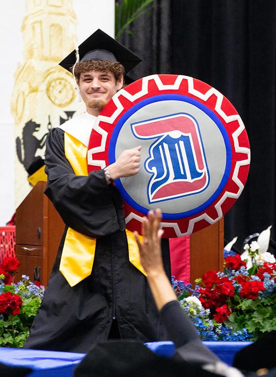 The student who served as Tommy Titan walks across the Commencement stage with Tommy's shield.
