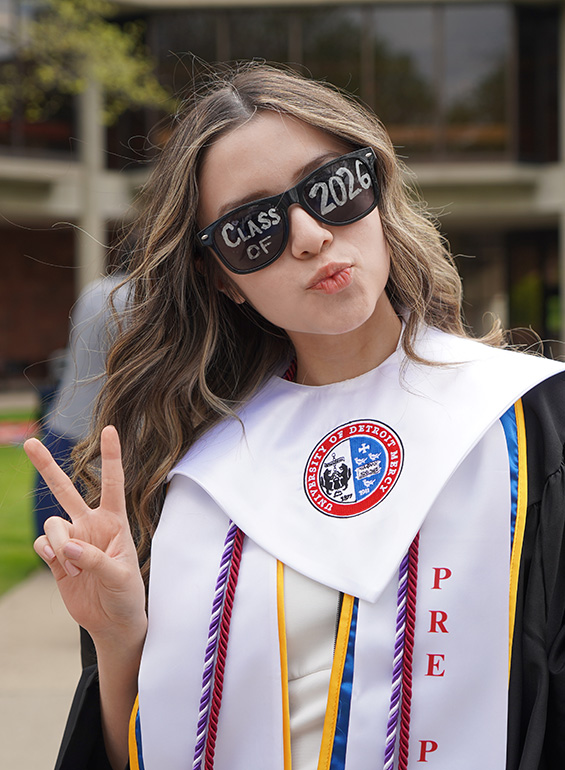 a graduate uses the peace sign while taking a photo wearing Class of 2026 classes.